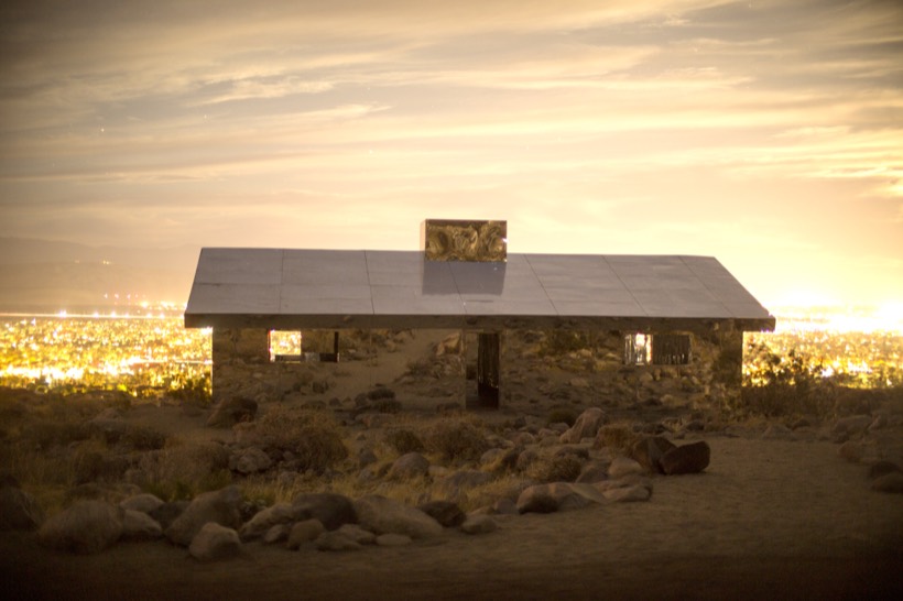 A mirrored desert house above the valley at dusk, city lights spread out below