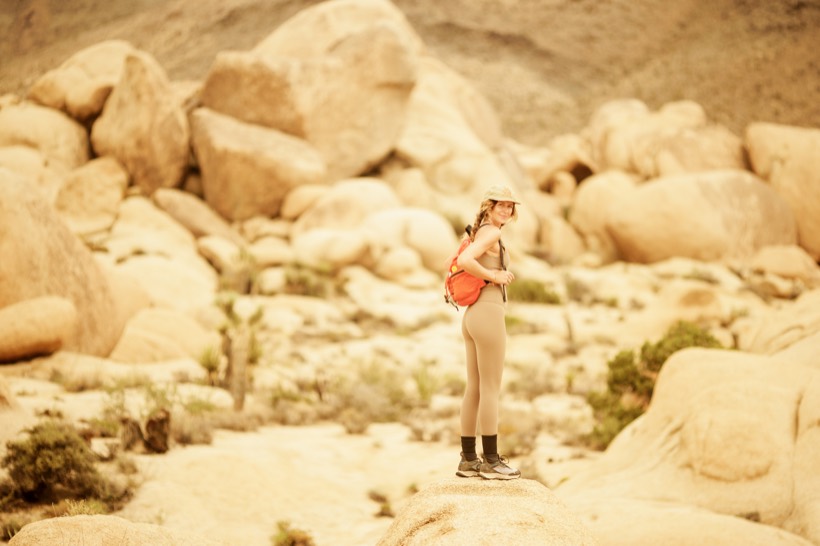 A hiker with an orange daypack standing among pale granite boulders
