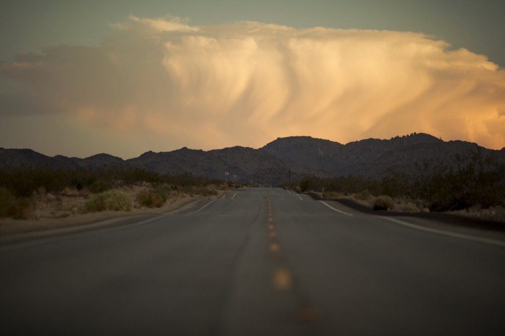 A storm cloud lit orange above a desert road