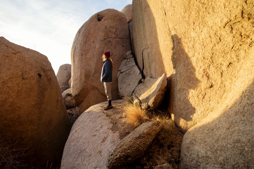 A figure standing on a sunlit ledge below a tall boulder