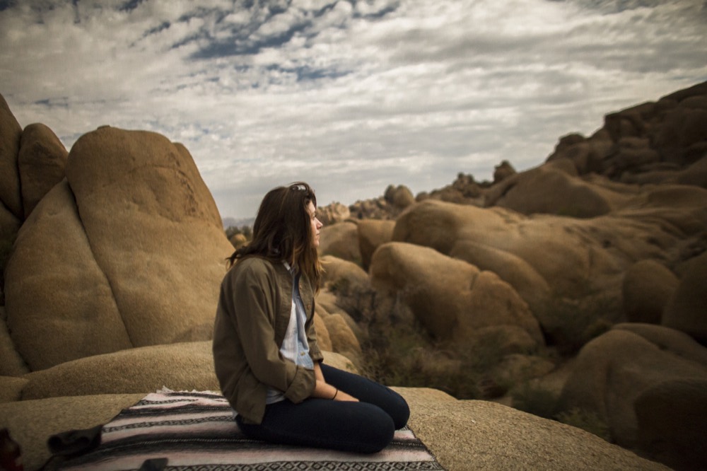 A person seated on a blanket on the rocks, looking out over the boulders