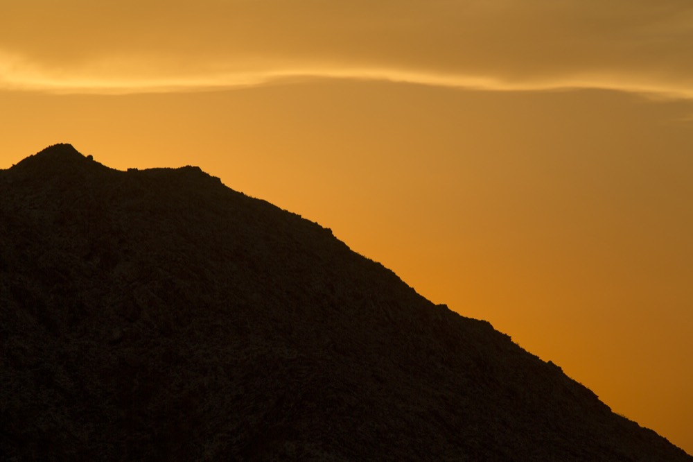 A mountain ridge in silhouette against an orange sky
