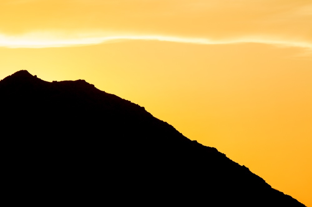 A mountain ridge in silhouette against a yellow sky