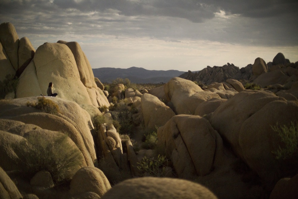 A figure seated among boulders in the evening light