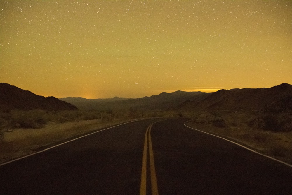 An empty road running toward the mountains under a glowing sky