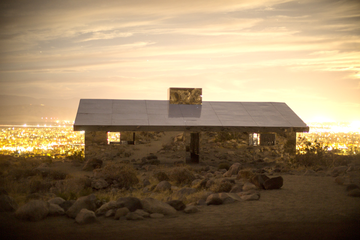 A mirrored desert house above the valley at dusk, city lights spread out below