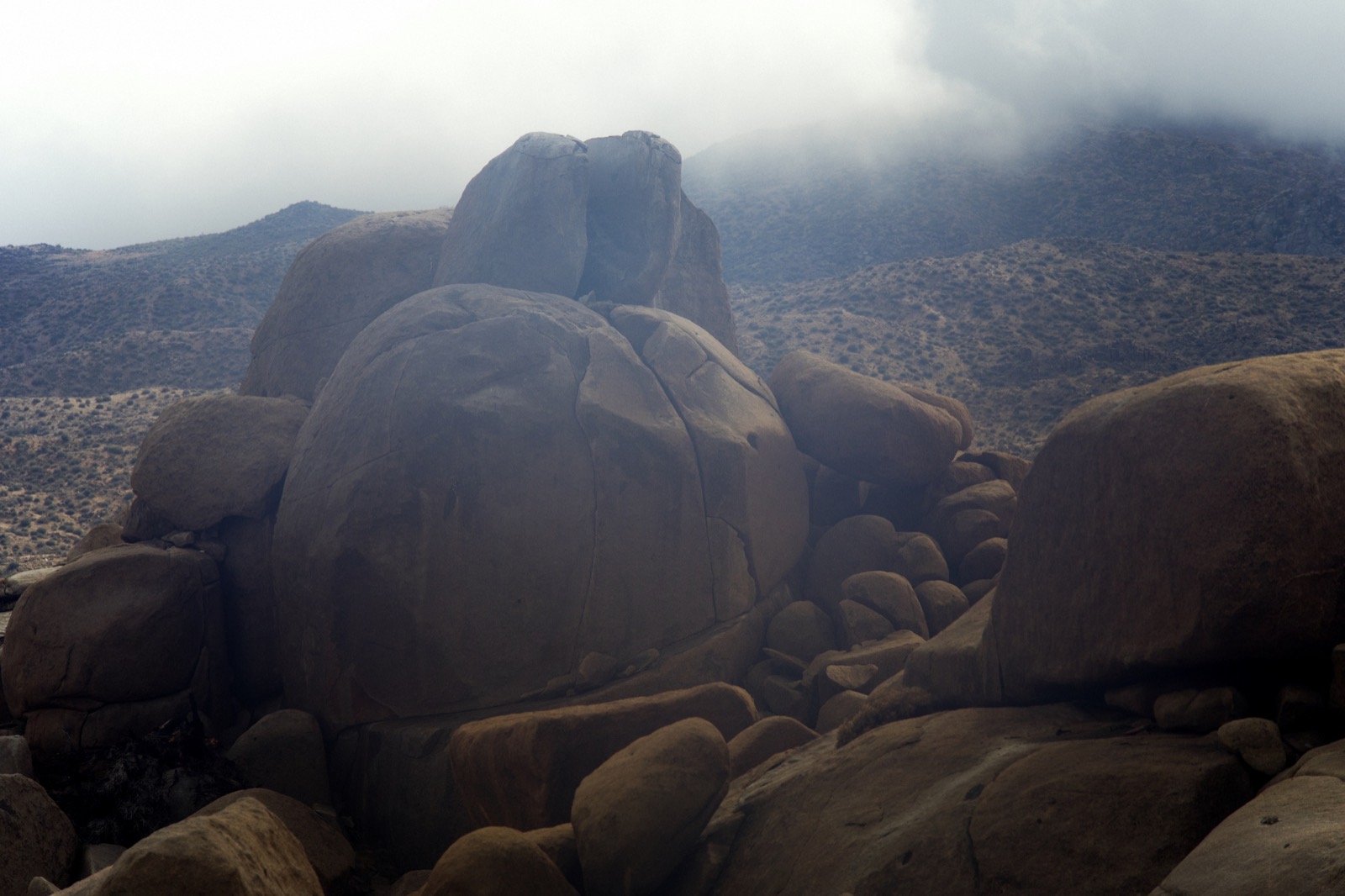 Stacked granite boulders under low cloud rolling across the desert hills