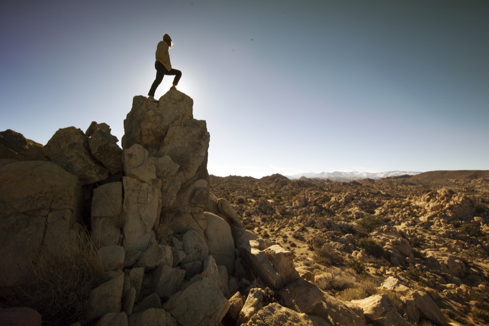 A climber standing on top of a granite tower above a wide boulder field