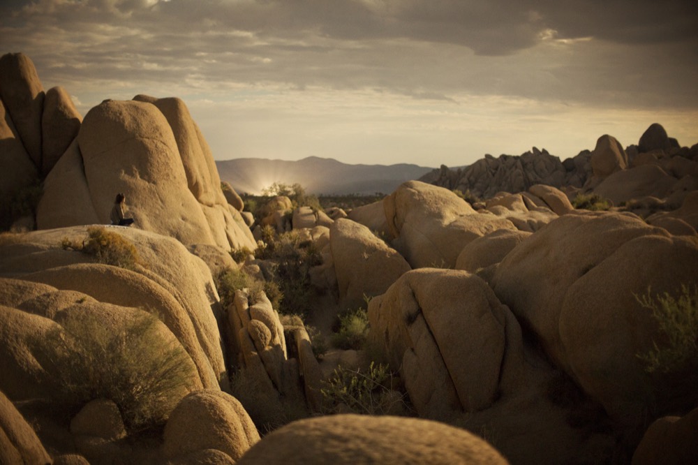 A figure seated high among boulders at golden hour