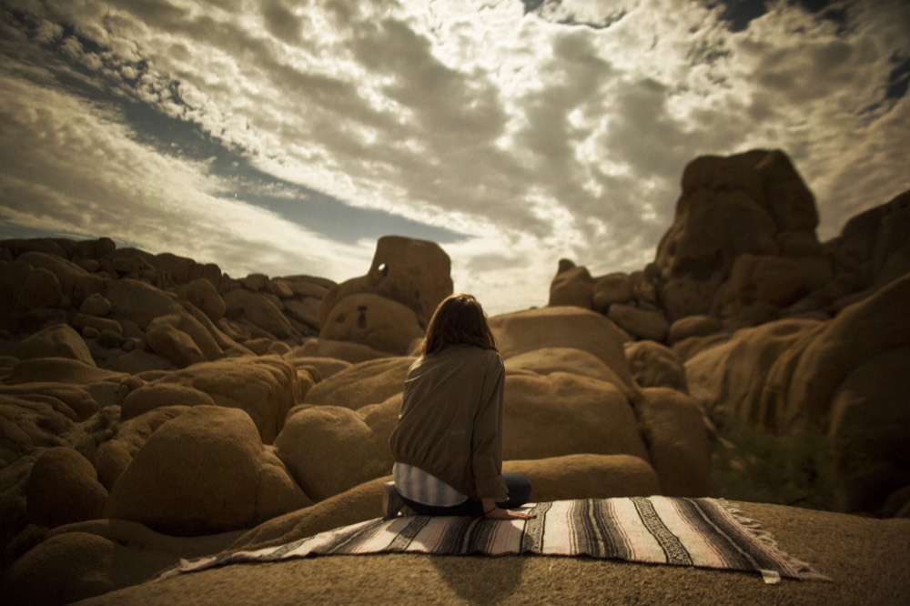 A person on a blanket on the rocks under a big, cloudy sky