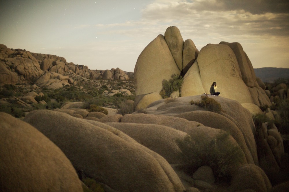 A climber perched on a granite dome in a field of boulders
