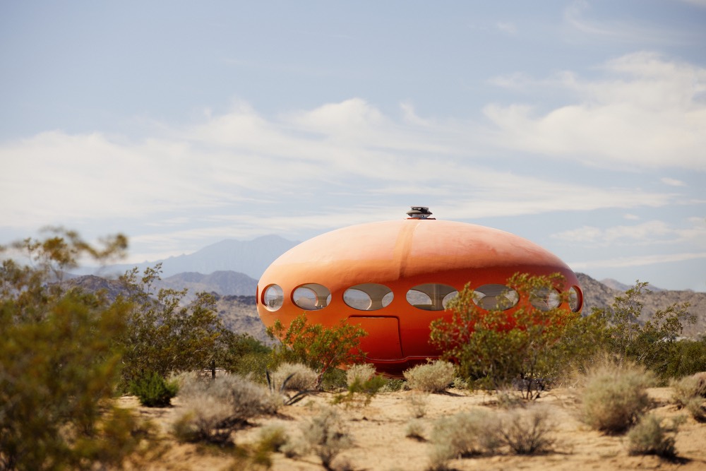 A round orange Futuro house among desert shrubs