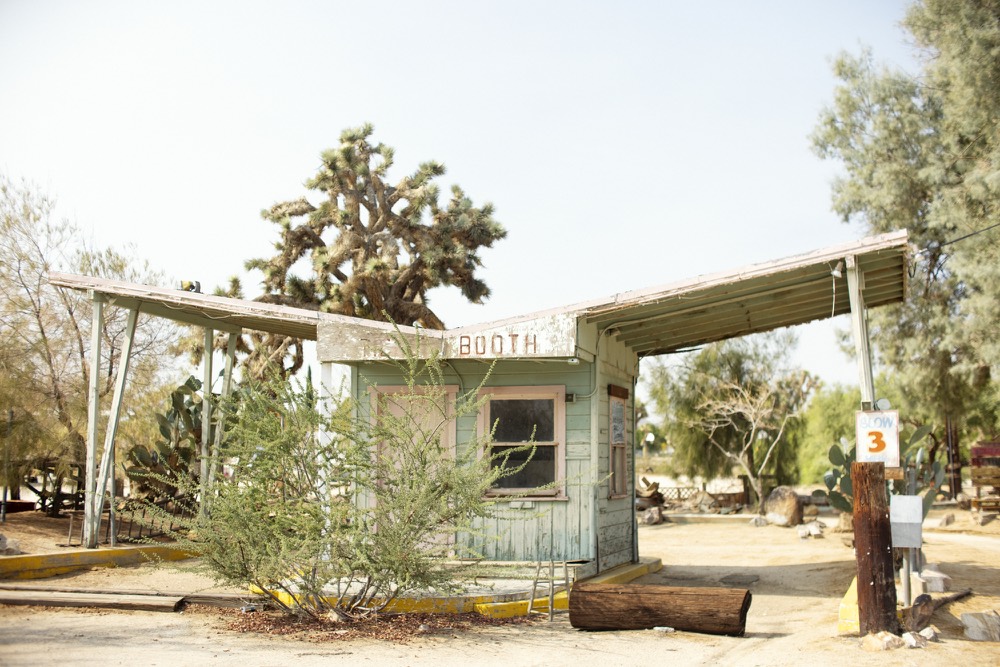 An old roadside booth with a sweeping roof, shaded by desert trees